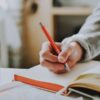 person holding on red pen while writing on book