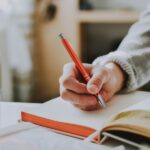 person holding on red pen while writing on book